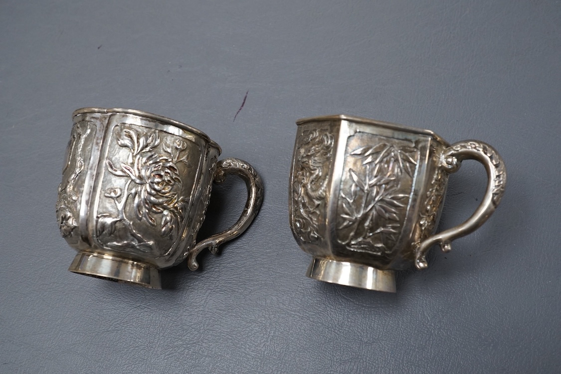 Two late 19th/early 20th century Chinese Export white metal tea cups, maker Wing Fat, embossed with bamboo, chrysanthemums and figures, of hexagonal or cusped form, 5.4oz.